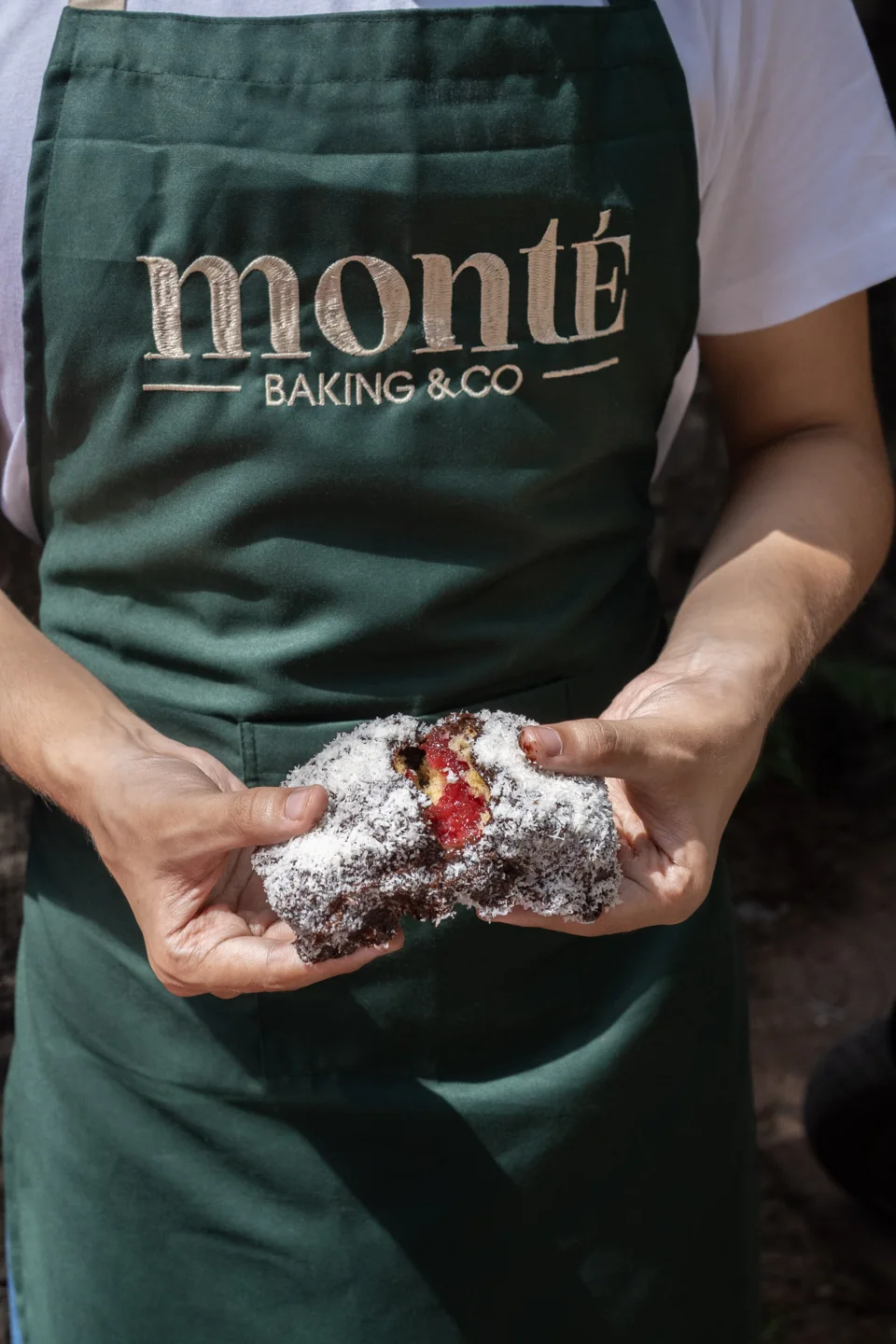 A baker in a Monté apron holding a baked treat
