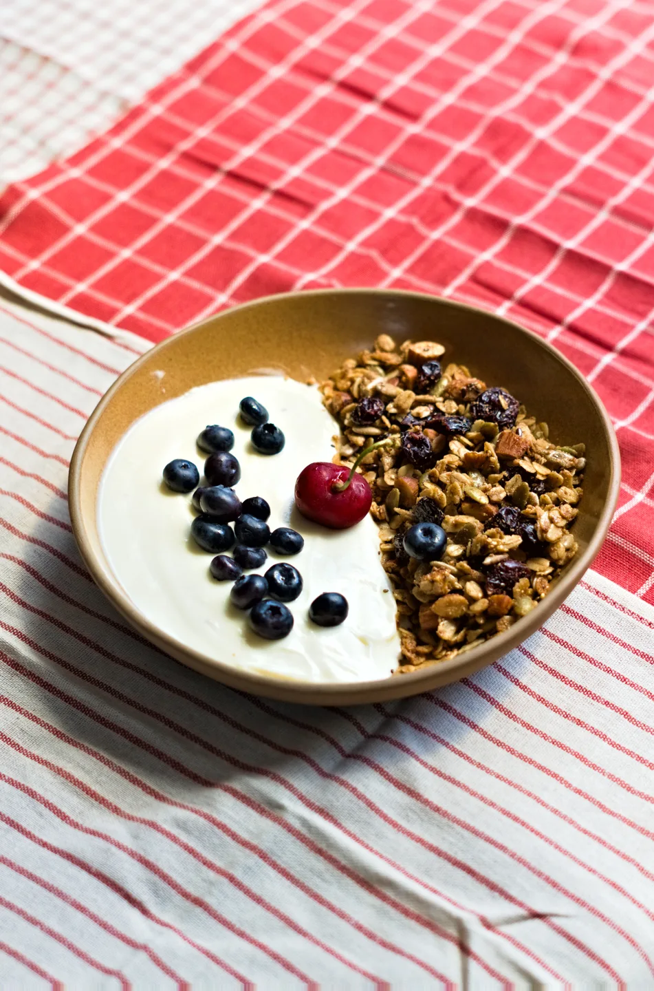 A breakfast bowl with fruit and granola on a checked tablecloth